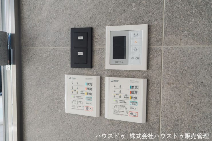 壁に美しく収まる換気・乾燥機の操作パネルと、サウナメーカーMETOSの操作パネル 。