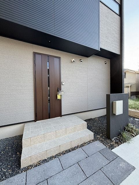 ダークトーンの壁面と木目調のドアがスタイリッシュな玄関♪アプローチには玉砂利が敷かれ、落ち着いた雰囲気を演出しています♪