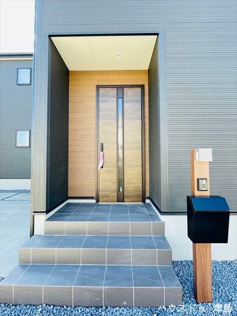 玄関ポーチは照明付きで暗い時間帯の帰宅も安心。表札・インターホン・ポストが一体型になった門柱。