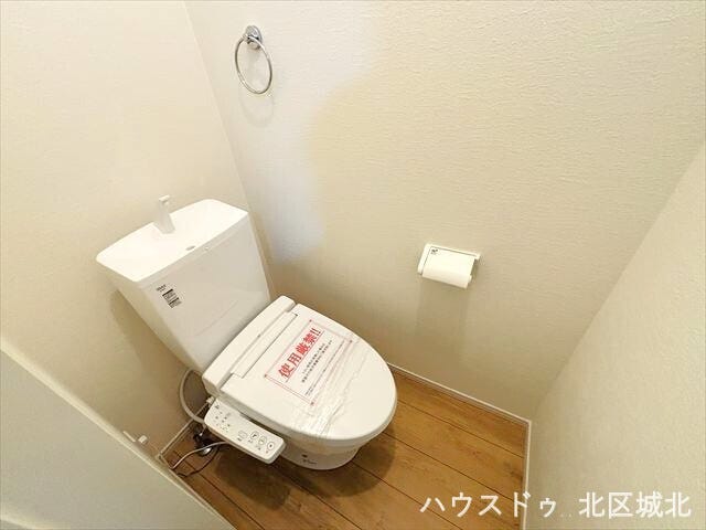 温水洗浄便座付きの清潔感あふれるトイレ。木目調の床が温かみを添え、落ち着いた空間を演出します。