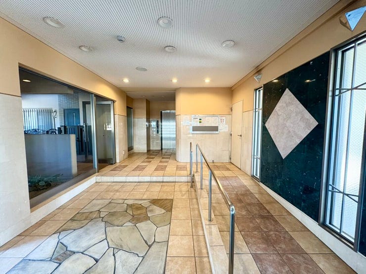 タイル張りの明るく清潔感のあるエントランスです。手すり付きのスロープがあり、ベビーカーやご高齢の方にも配慮された共用空間です。管理状況の良さも感じられます。