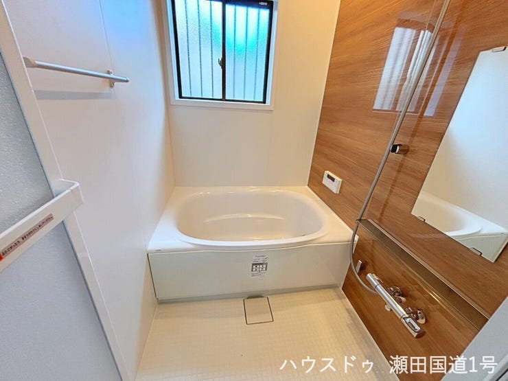 壁の一面に施された木目調のアクセントウォールが、空間に温かみとモダンな印象を与えます。白い浴槽と壁が清潔感を際立たせ、リラックスできる落ち着いた空間を演出します。