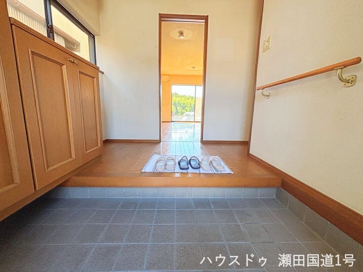 室内奥の部屋からの光(または窓からの光)が差し込み、明るく開放的なエントランスを演出しています。清潔感のあるタイルと木目調の組み合わせも好印象です。