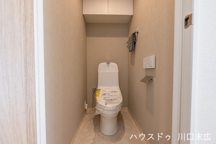 温水洗浄便座を備えた清潔感のあるトイレ。上部には吊戸棚が設置されており、トイレットペーパーや掃除用品などをストックしておくのに便利です。