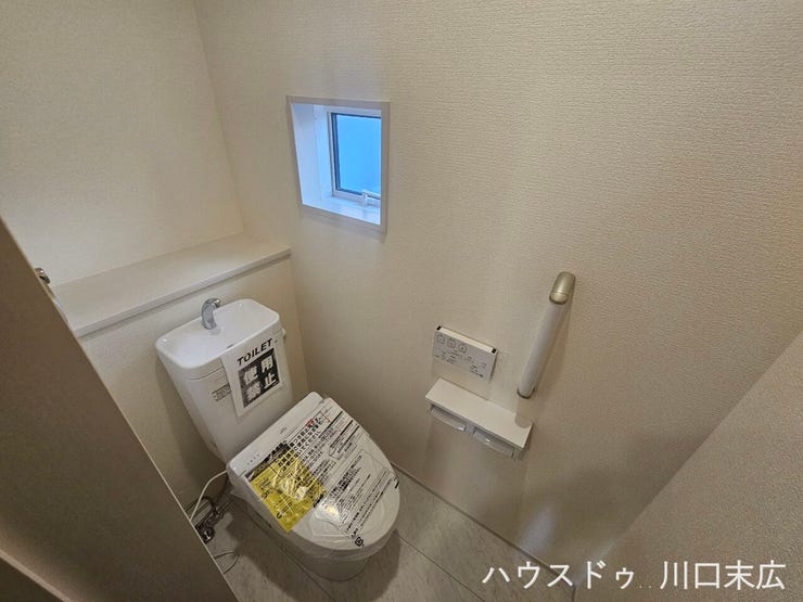 温水洗浄便座を備えた清潔なトイレスペース。手すりが設置されており、立ち座りの動作をサポートするなど、安全性にも配慮された設計です。