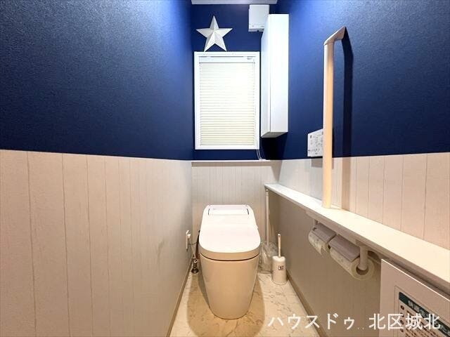 ブルーのアクセントクロスが映えるおしゃれなトイレ空間。手すり付きで使い勝手も良く、デザイン性と快適性を兼ね備えた清潔感のあるスペースです。