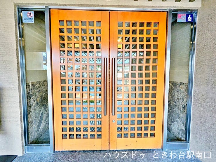 木調デザインのダブルドアが採用されたエントランス。外部からの視線をやわらかく遮りつつ、建物の品格を感じさせる落ち着いた雰囲気を演出しています。
