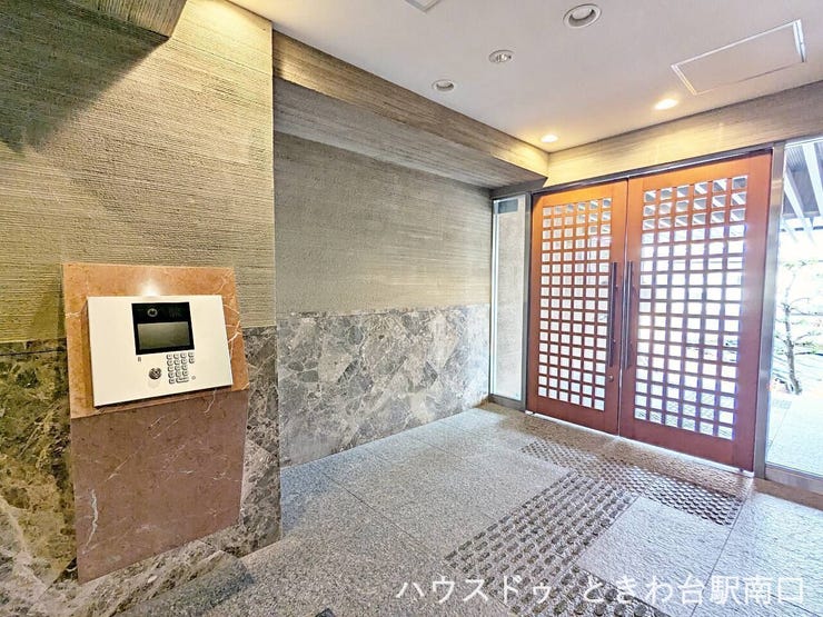 オートロック付きのエントランスは、落ち着いた色合いの壁面と石調タイルでまとめられ、清潔感のある空間です。格子デザインの扉から自然光も入り、来訪者を明るく迎え入れます。