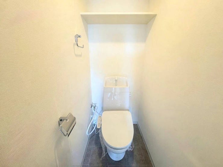 清潔感あふれるシンプルなトイレ空間です。手洗い一体型タンクと温水洗浄便座を装備しており、上部にはペーパーや清掃用品の保管に便利な棚が設置されています。