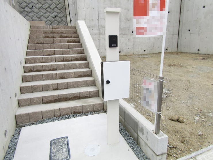 段差を活かしたアプローチが印象的な住まい。道路面より一段上がった設計で、外からの視線にも配慮されています。すっきりとした門柱とポストが、清潔感のある外観を引き立てます。