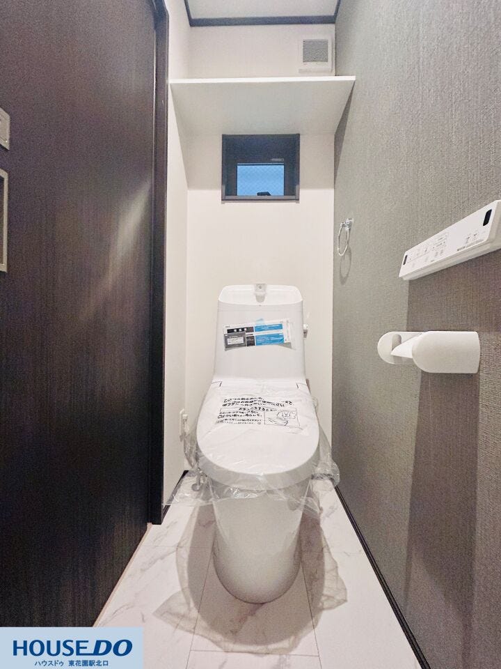 1階のトイレはグレーのアクセントクロスが落ち着いた雰囲気を演出。清掃性が高く、日々のお手入れがスムーズです。小窓からの採光と換気機能、上部の棚など、使い勝手に配慮した設備が整っています。
