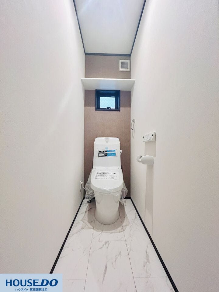 2階のトイレは木目調クロスが温かみを感じさせる、奥行きのある空間です。1階と同様に温水洗浄便座やスマートなリモコンを完備。予備のペーパーや掃除用品を置ける収納棚もあり、機能的な空間が確保されています。