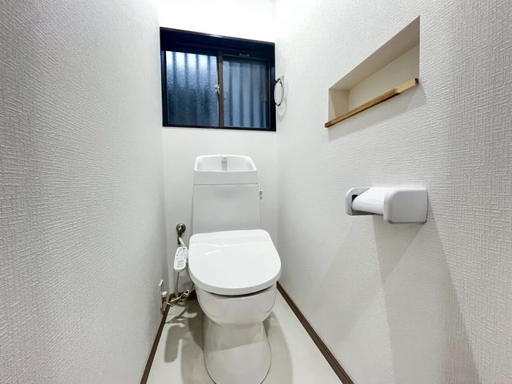 白を基調としたトイレ空間です。奥には換気や自然採光が可能な窓が配置されています。側面の壁にはニッチ棚が設けられており、小物類の配置が可能です。手洗い器一体型の便器が備わる設計となっています。