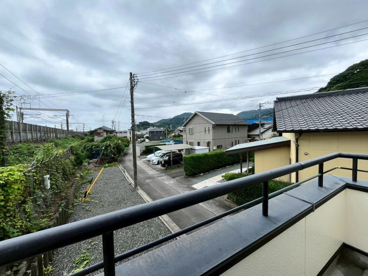 目の前には道路が通り、周辺には戸建て住宅が立ち並んでいます。左手には線路があり、遠方には山並みを望むことができます。