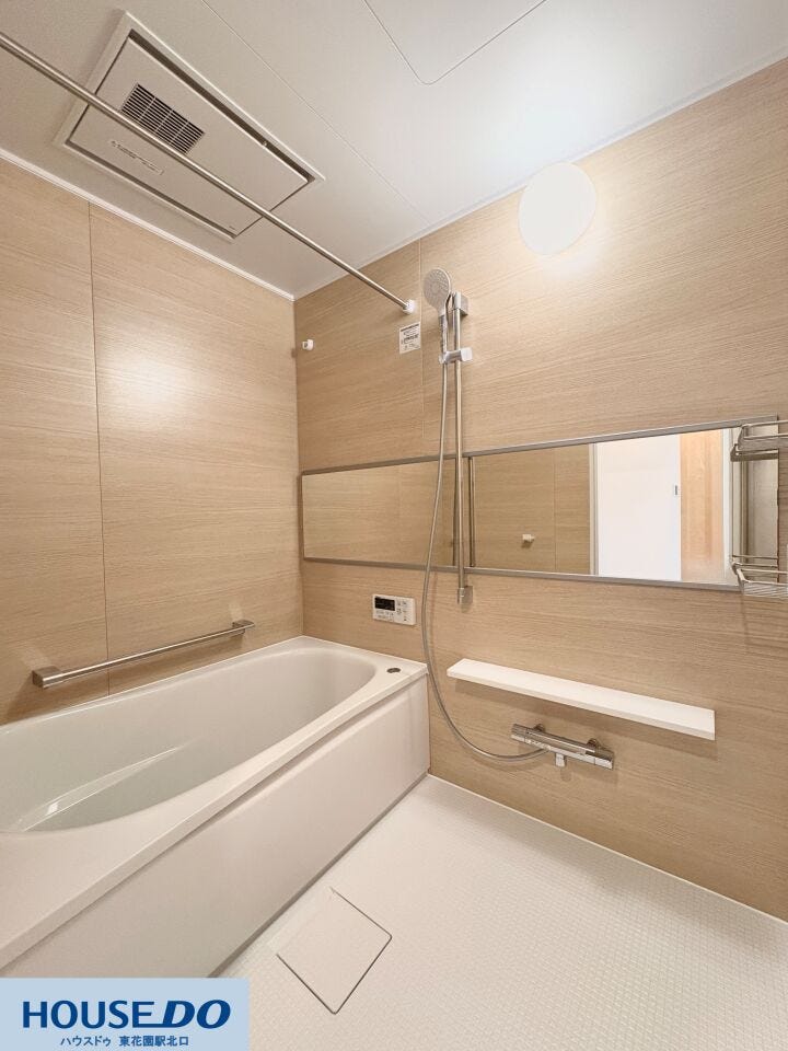 木目調のパネルが落ち着いた印象を与える浴室です。雨の日の衣類乾燥に便利な浴室乾燥機や、横長で空間を広く見せるミラーを設置。手すりも備わっており、どなたでも安心して入浴を楽しめる配慮がなされています。