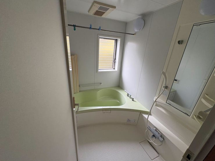 ゆったりとした曲線デザインの浴槽を備えたユニットバスです。浴室乾燥機とランドリーパイプがあり、天候を問わず洗濯物を干せます。手すりや換気用の小窓も備わっており、安全性と衛生面に配慮された造りです。