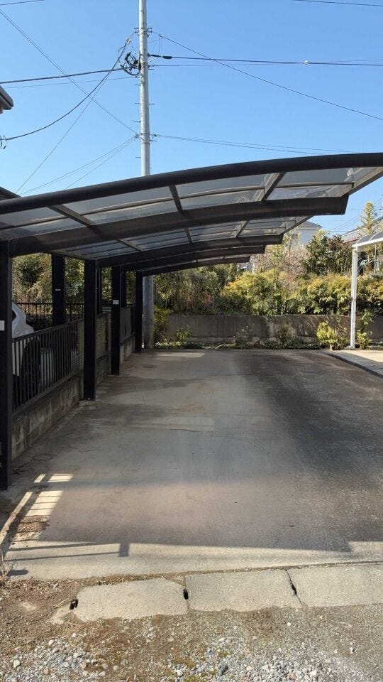 カーポート付きの駐車スペースを確保しており、雨の日でもスムーズに乗り降りが可能です。前面道路はゆとりがあり、車の出し入れも落ち着いて行えます。青空に映えるモダンな外観が特徴的な戸建て住宅です。