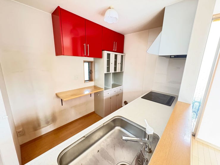 赤色の吊り戸棚がアクセントの対面式キッチンです。IHクッキングヒーターを採用しており、お手入れが容易です。背面には収納棚やカウンターが設置されているため、家電の配置や調理作業に活用いただけます。