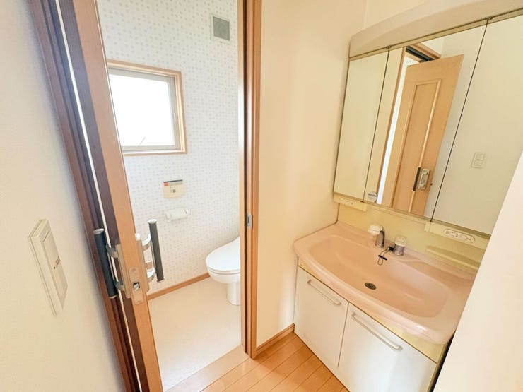 洗面化粧台は三面鏡を採用しており、鏡裏に小物を収納できます。隣接するトイレには小窓があるため、自然光を取り入れながら換気が可能です。どちらも白を基調とした清潔感のある内装でまとめられています。