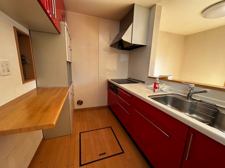 赤色の吊り戸棚がアクセントの対面式キッチンです。IHクッキングヒーターを採用しており、お手入れが容易です。背面には収納棚やカウンターが設置されているため、家電の配置や調理作業に活用いただけます。