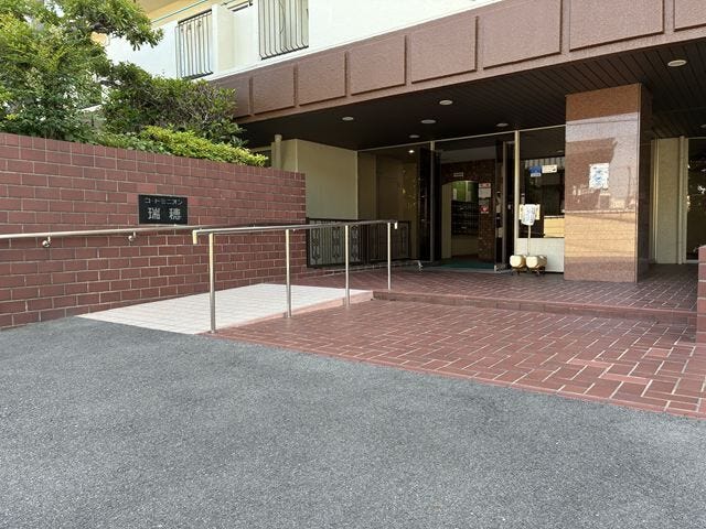 スロープと手すりが設置され、ベビーカーや車椅子でもスムーズに移動できるバリアフリーなマンションエントランス