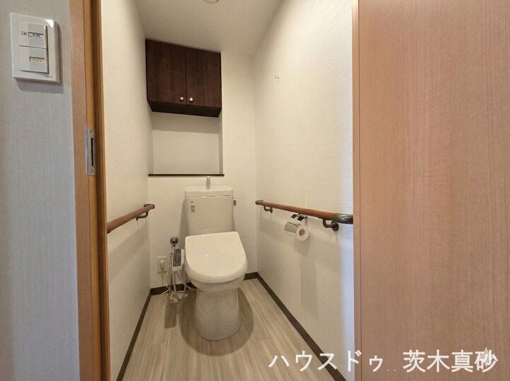 【手すり付きで安心・清潔感のあるトイレ空間】
両サイドの壁に手すりを設置し、毎日の動作を優しくサポート。
便利な吊り戸棚収納を備えた、木目調が温かい落ち着く空間です。