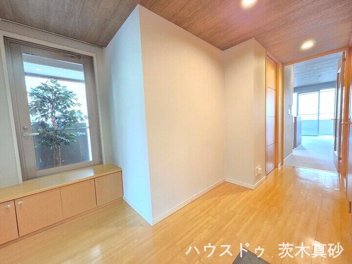 【自然光が差し込む、開放感あふれる広々とした廊下】
玄関前の大窓から外の光を取り込む明るい空間。
便利なローボード収納を備え、木目調の天井が温もりを演出します。