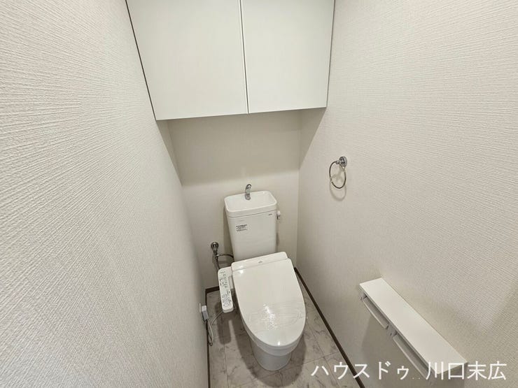 手洗い器付きのタンクを備えた、使い勝手の良いトイレ空間です。上部には扉付きの吊り戸棚を設置しており、トイレットペーパーなどの備品を人目に触れず収納できます。
