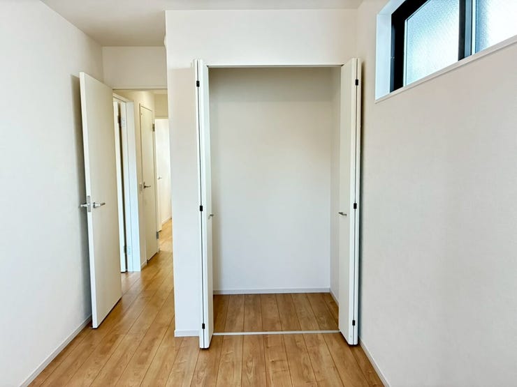扉が大きく開く、使い勝手の良いクローゼットを備えた洋室です。高めの位置に配された窓が、プライバシーを守りながら光を取り込みます。温かみのある床材とも調和し、生活感を隠してすっきりと快適に過ごせます。