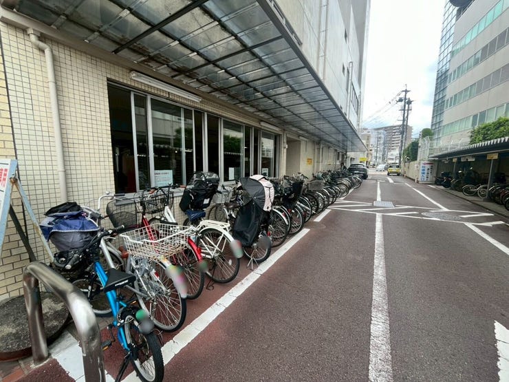 建物の壁面に沿って白線で区画分けされた平置きタイプの駐輪場です。上部には屋根が設けられ、雨天時の影響を軽減する構造です。