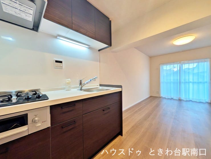 南向きの大きな窓から陽光が降り注ぐ、明るいLDK。ダークブラウンのキッチンが空間を引き締め、モダンな印象を与えます。
