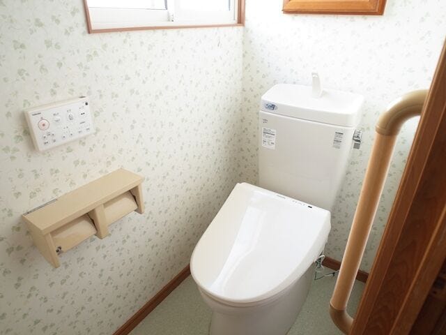 手洗い器付き温水洗浄便座のトイレ。手すり付きで立ち座りもラク。小さな葉柄クロスと木目の建具が、素朴で温かみのある雰囲気をつくります。