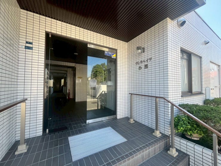 白いタイル張りの外壁と、ダークトーンの床や天井のコントラストが印象的なマンションのエントランスです