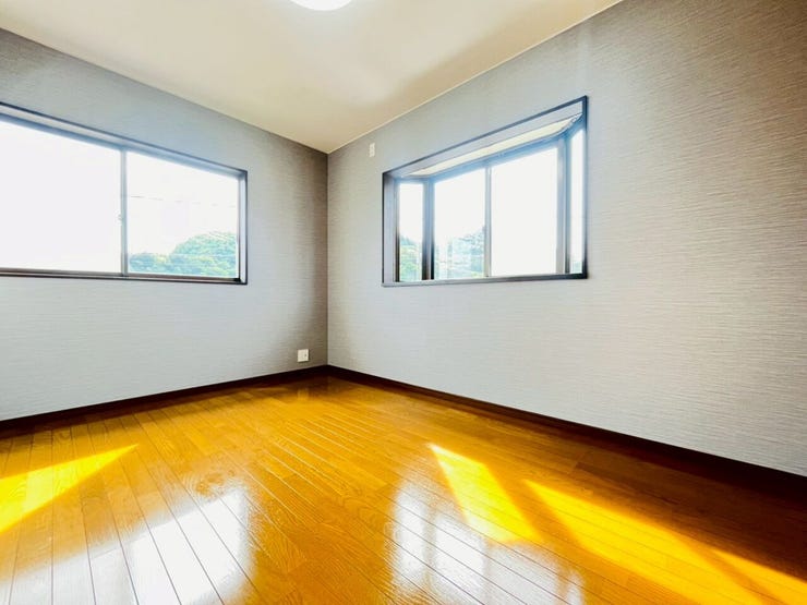 落ち着いたグレー系のアクセントクロスが、洗練されたモダンな雰囲気を演出しています。二面に窓が配置されており、日差しがフローリングに心地よく反射する明るい室内です。