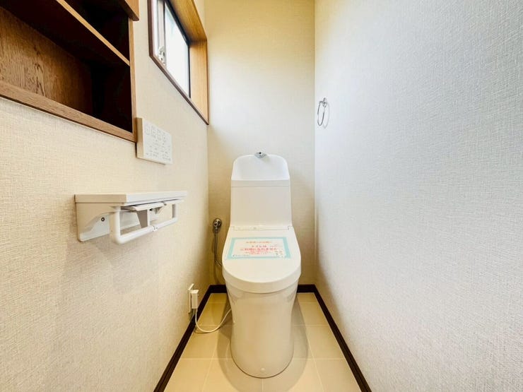 清潔感のある白を基調とした、スッキリとした印象のトイレです。温水洗浄便座が備わっているほか、小物を置ける棚や窓も配置されており、実用性と換気への配慮が感じられます。