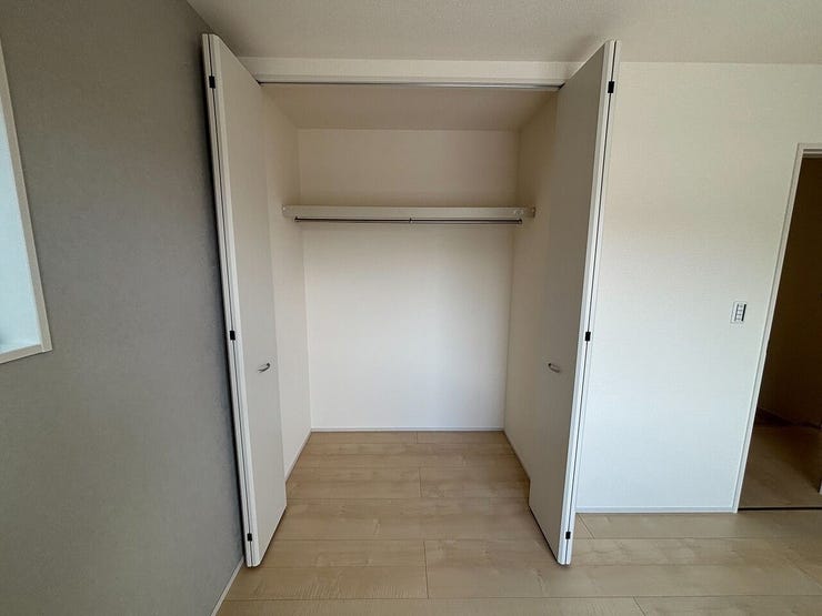 開口部が広い折れ戸が採用されたクローゼットです。内部にはハンガーパイプと枕棚が備わっており、衣類の吊り下げや上部の空間を活用した整理に対応します。左側の壁面にはアクセントクロスが施されています。