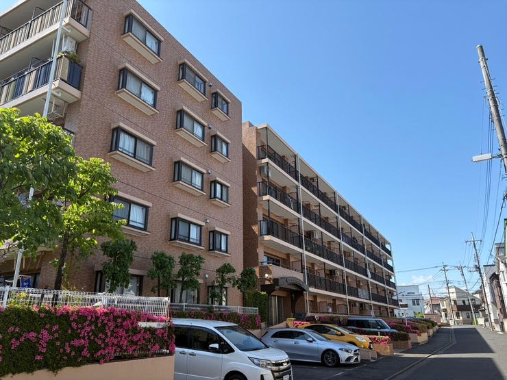 ブラウンのタイルが青空に映える、落ち着いた佇まいのマンション。周囲には遮るものがなく、陽当たりや通風の良さが外観からも伝わってきます。植栽の緑に囲まれたエントランスが、住まう人を優しく迎えます。