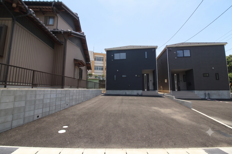 広々とした前面道路で車の出し入れもスムーズ。モダンな黒の外観が2棟美しく並ぶ、開放感あふれる新築です。