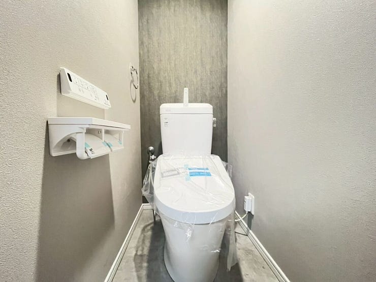 背面にグレー調のアクセントクロスを採用したトイレスペースです。壁面には温水洗浄便座の操作パネルが設置されています。