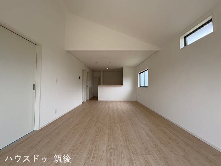 【勾配天井が広がりを演出するLDK】上部へと高くなる天井設計により、空間に心地よい奥行きが生まれます。高い位置に設置された高所窓から、室内の奥まで優しい自然光が差し込む明るいリビングダイニングです。