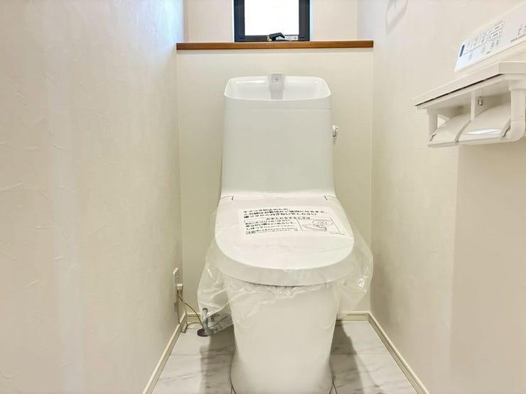 白を基調とした清潔感あふれるトイレスペースです。快適な温水洗浄便座や手洗い付きタンク、便利な2連ペーパーホルダーを完備。奥には換気や採光に役立つ小窓とカウンターがあり、心地よく使える設計です。