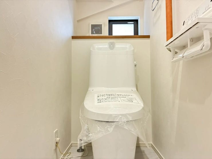 白を基調とした清潔感あふれるトイレスペースです。快適な温水洗浄便座や手洗い付きタンクを完備。奥には換気や採光に便利な小窓とカウンターを配し、空間を有効活用した落ち着きのある設計です