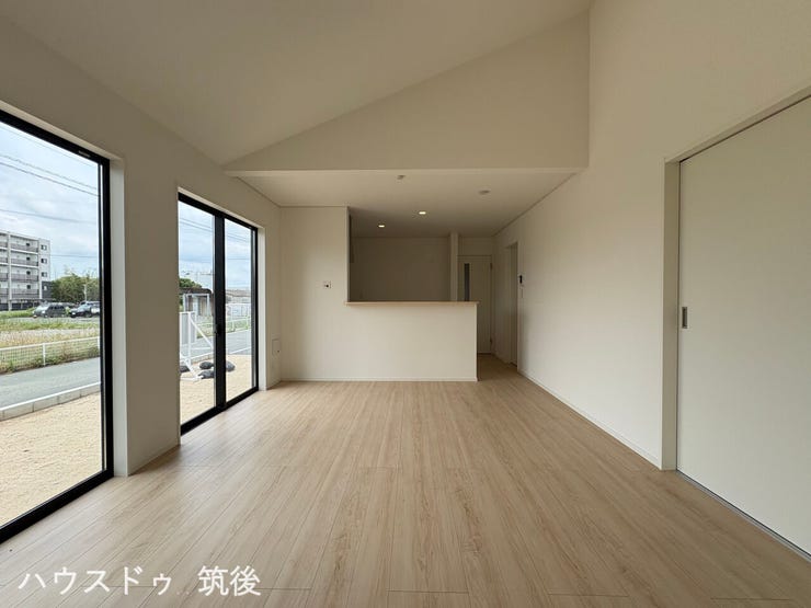【高天井が特徴の16帖LDK】開放感のある勾配天井を採用したリビングです。奥にはご家族との会話が弾む対面式のシステムキッチンを配置。大きな窓が並び、室内にしっかりと自然光を採り込める設計です。