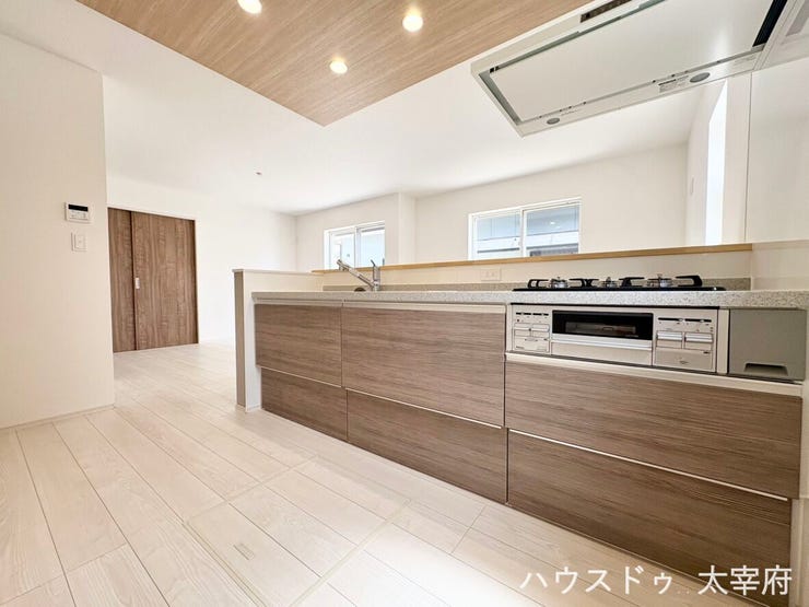 システムキッチンの収納扉や下がり天井の部分に温かみのある木目調のデザインが採用されており、明るく清潔感のある白を基調とした空間に、ナチュラルで洗練されたアクセントを加えています。