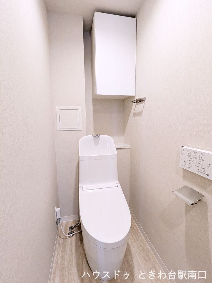 清潔感のある白で統一された温水洗浄便座付きのトイレです。上部には備品の保管に便利な吊戸棚が設置されており、限られたスペースを有効に活用できるすっきりとした設計となっています。