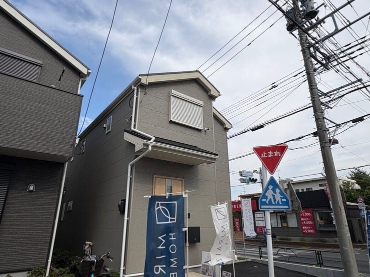 見通しのよい前面道路に面しており、お車の出し入れや駐車がスムーズにできる角地。淡いグレーの外壁とナチュラルな木目調の玄関ドアが、やさしい表情を見せます。開放的な空が広がる、心地のよい佇まいです。