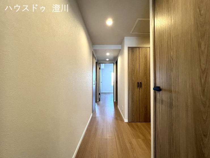 温かみのある木目調の建具とフローリングが美しい廊下。すっきりとしたダウンライトが明るく上品な雰囲気を演出し、便利な廊下収納も完備しています。