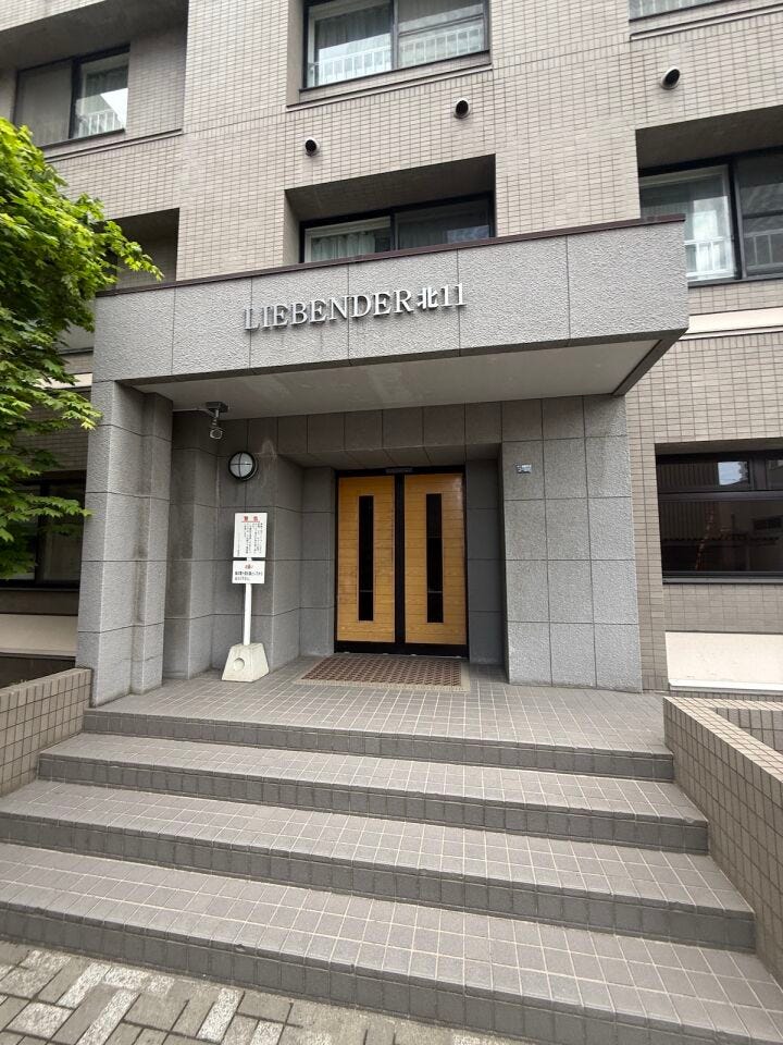 木目調の扉がアクセントのモダンなエントランス。防犯カメラ完備でセキュリティにも配慮されています