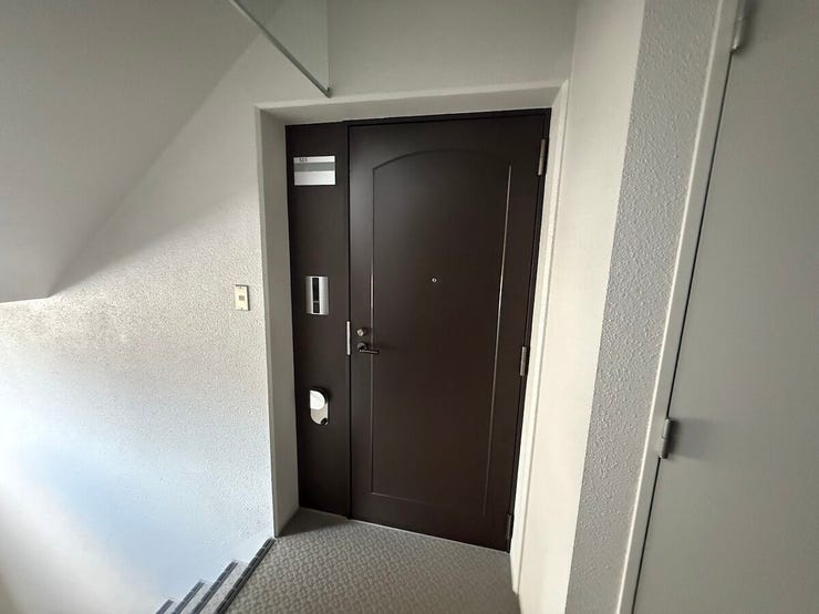 白を基調とした壁紙に、ダークカラーの玄関ドアが映えるモダンなコントラスト