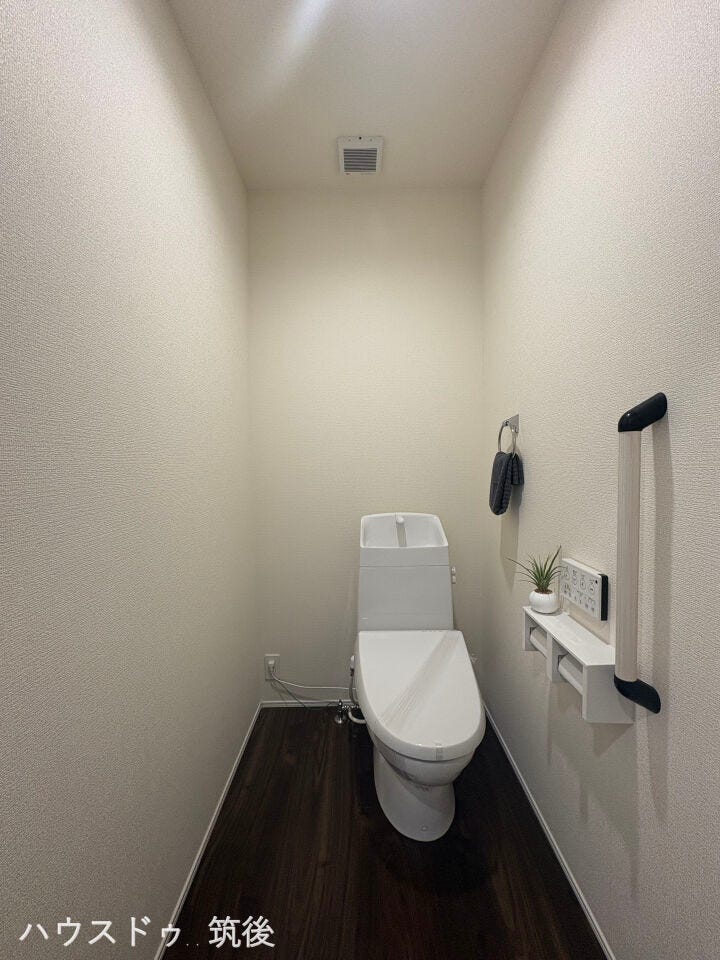 【快適で優しい設計のトイレ】手洗い付きの温水洗浄一体型トイレです。壁面には立ち座りをサポートする手すりを設置し、シニア世代や小さなお子様も安心。便利な小物置きカウンターも付いた快適空間です。